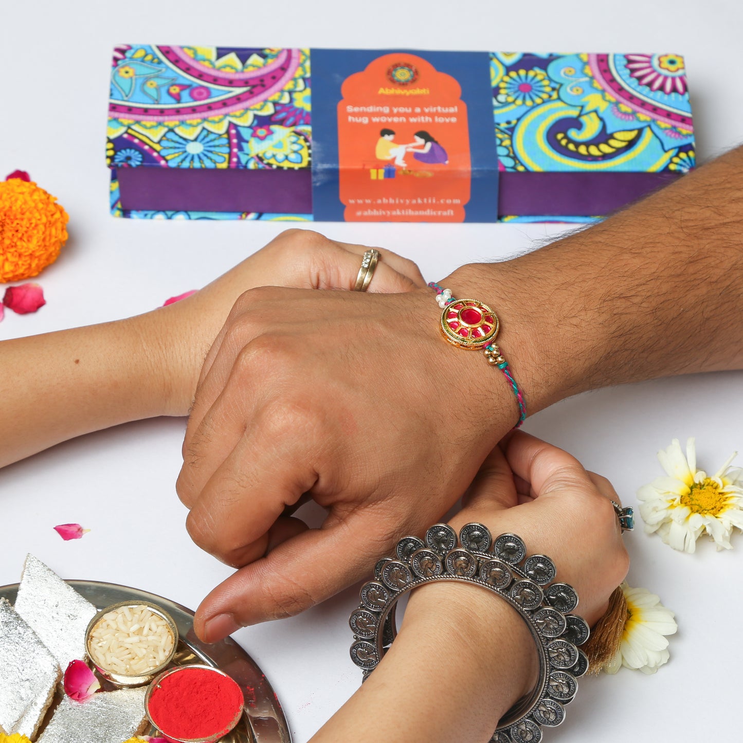 Rakhi bracelet featuring a flower, pearls, and red stone in a beautiful Rakhi hamper