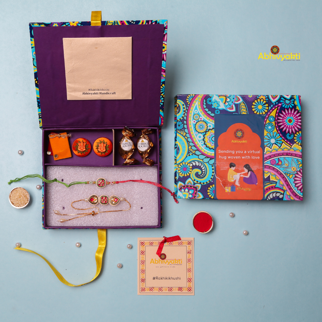 Decorative Rakhi Lumba are displayed on a light blue background. The top rakhi features a circular centerpiece with red and green enamel work, surrounded by small pearls and gold beads, and is tied with red and green threads. The bottom rakhi has three ornate elements: a central round motif with red and green enamel, flanked by two teardrop-shaped motifs with gold, red, and white detailing, finished with pearl accents and a gold chain clasp. Both rakhis have intricate traditional designs and embellish