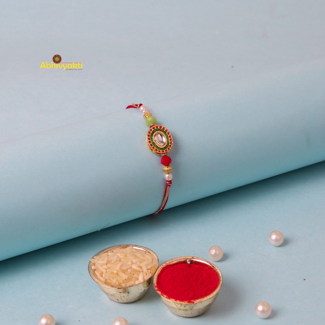 Kundan rakhi with red and green colors, adorned with gold and green stone and lovely beads