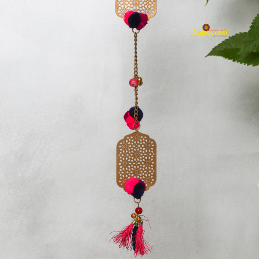 Filigree designed metallic door hanging with red and purple pom-poms, suspended against a blurred background