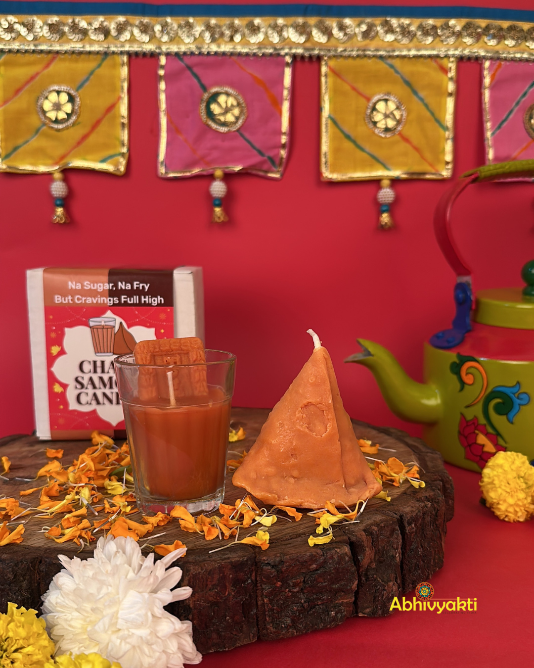 Decorative, usable soy candles shaped like a glass of chai with a biscuit and a triangular samosa, designed to look like popular Indian snacks