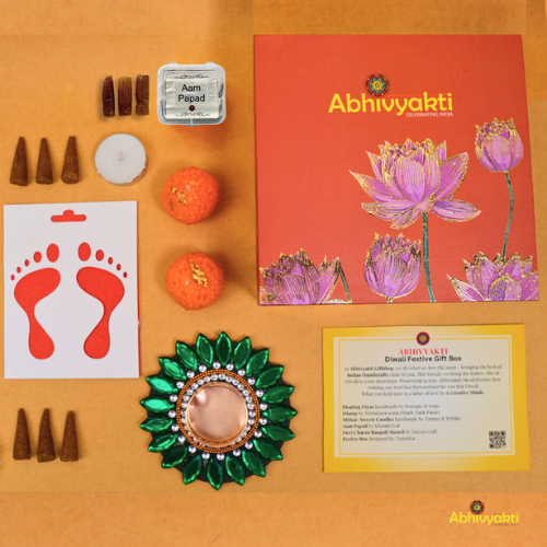 A festive Diwali hamper filled with an assortment of decorative items and treats. The hamper includes colorful floating diya, a box of mithai sweet candle, fragrant incense sticks, a small decorative toran, and festive Ganesh Lakshmi tealight alongwith tangy juicy mango roll up . The items are beautifully arranged in a festive box with vibrant, rich colors and intricate detailing, evoking the spirit of Diwali celebrations. The hamper is a perfect gift for the festive vibe