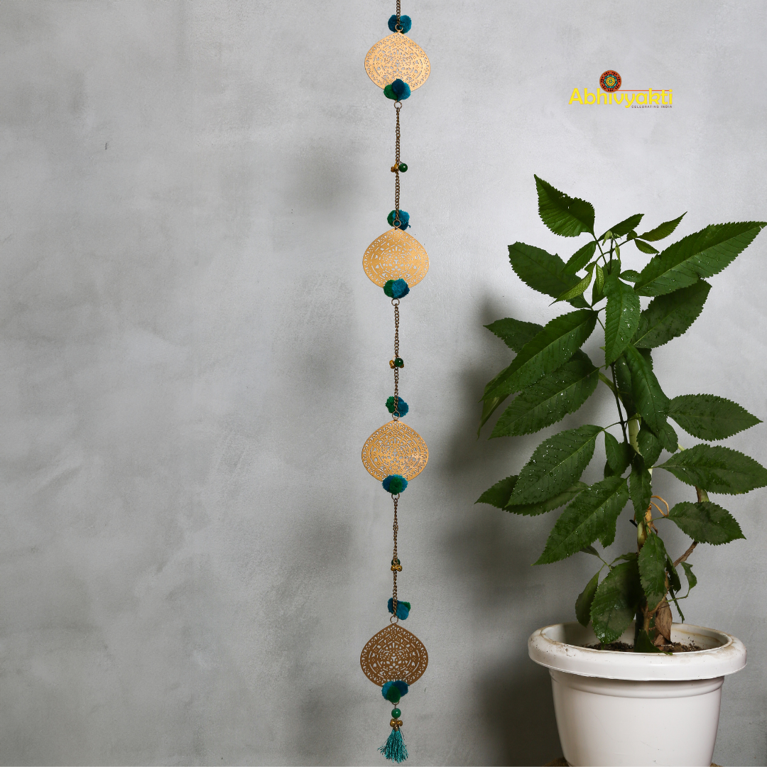 Filigree metal door hanging in a circular shape featuring detailed ornamental design, adorned with blue pom-poms and tiny golden bells, suspended from a chain indoors