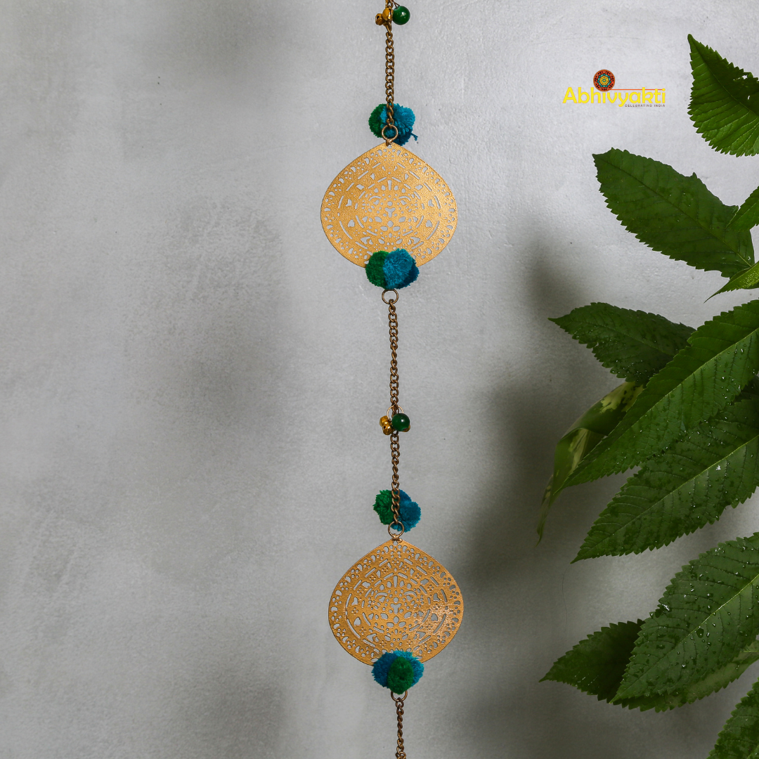 Filigree metal door hanging in a circular shape featuring detailed ornamental design, adorned with blue pom-poms and tiny golden bells, suspended from a chain indoors