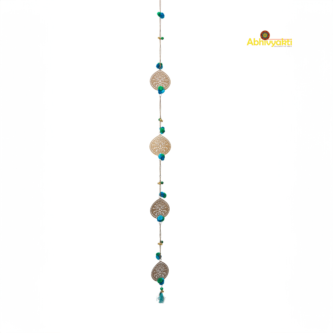 Filigree metal door hanging in a circular shape featuring detailed ornamental design, adorned with blue pom-poms and tiny golden bells, suspended from a chain indoors