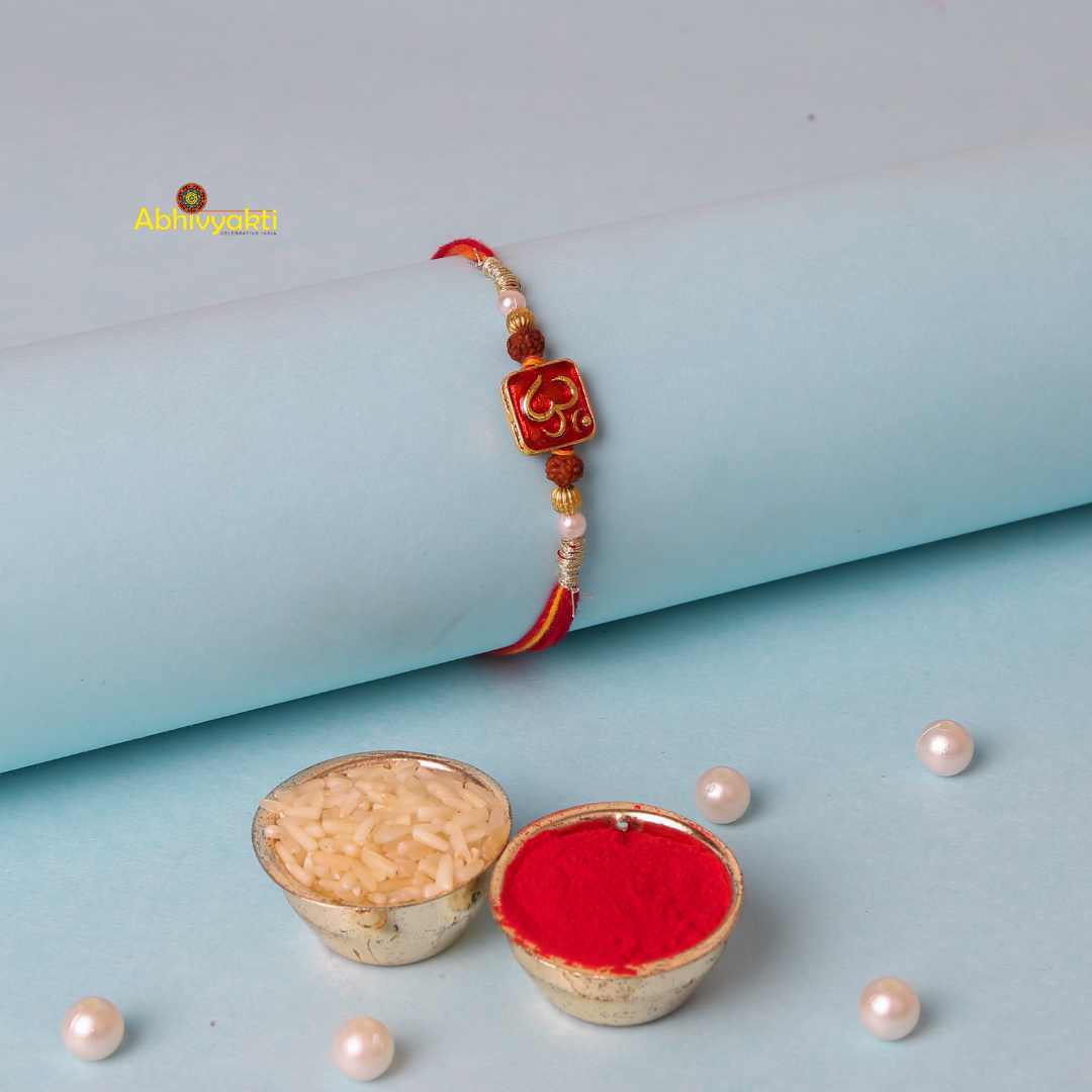 Om rakhi with beads, showcasing a red and yellow thread band adorned with golden and rudraksha beads, features a red square centerpiece with a gold "Om" symbol, displayed against a pastel blue background