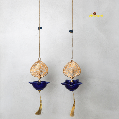 Two decorative hanging peacock swagata diya with gold leaf designs and blue bowls on a light gray background.