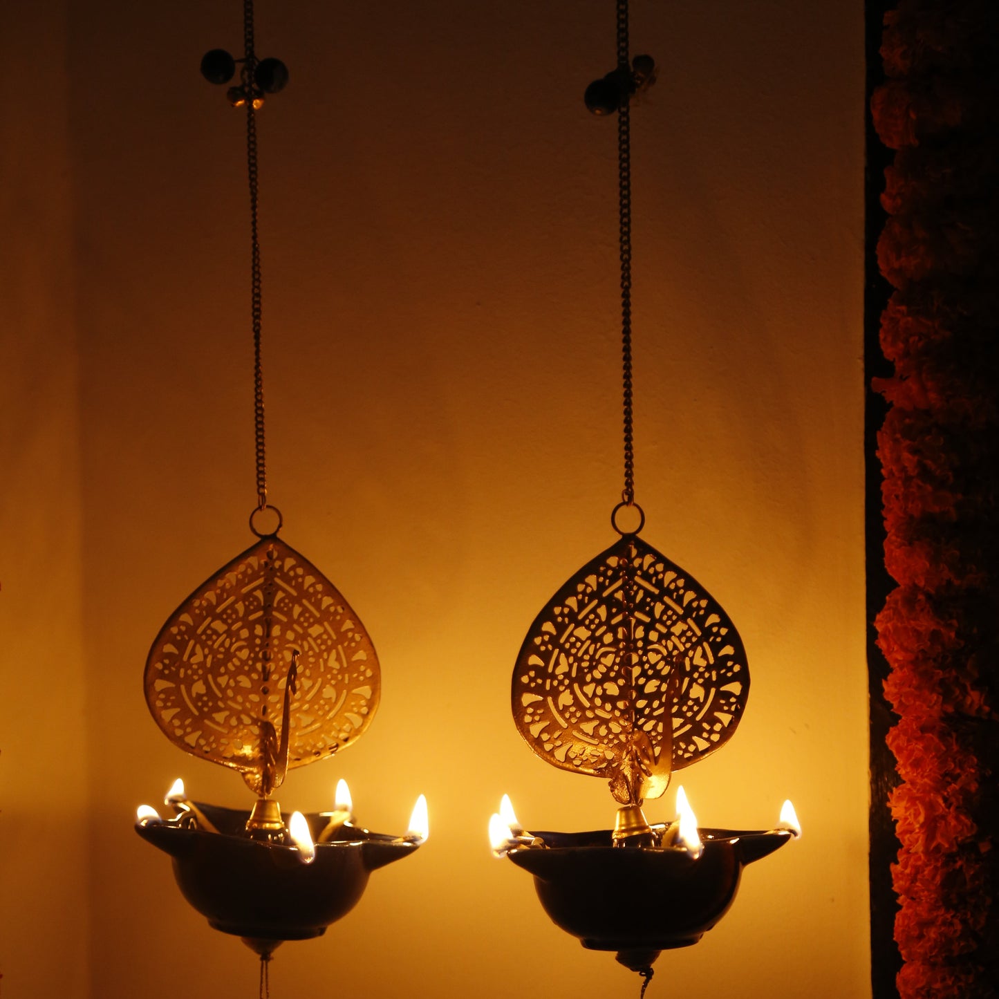 Decorative Peacock Swagata long chain T-light holder with intricate designs reflected on a surface, against a warm background.