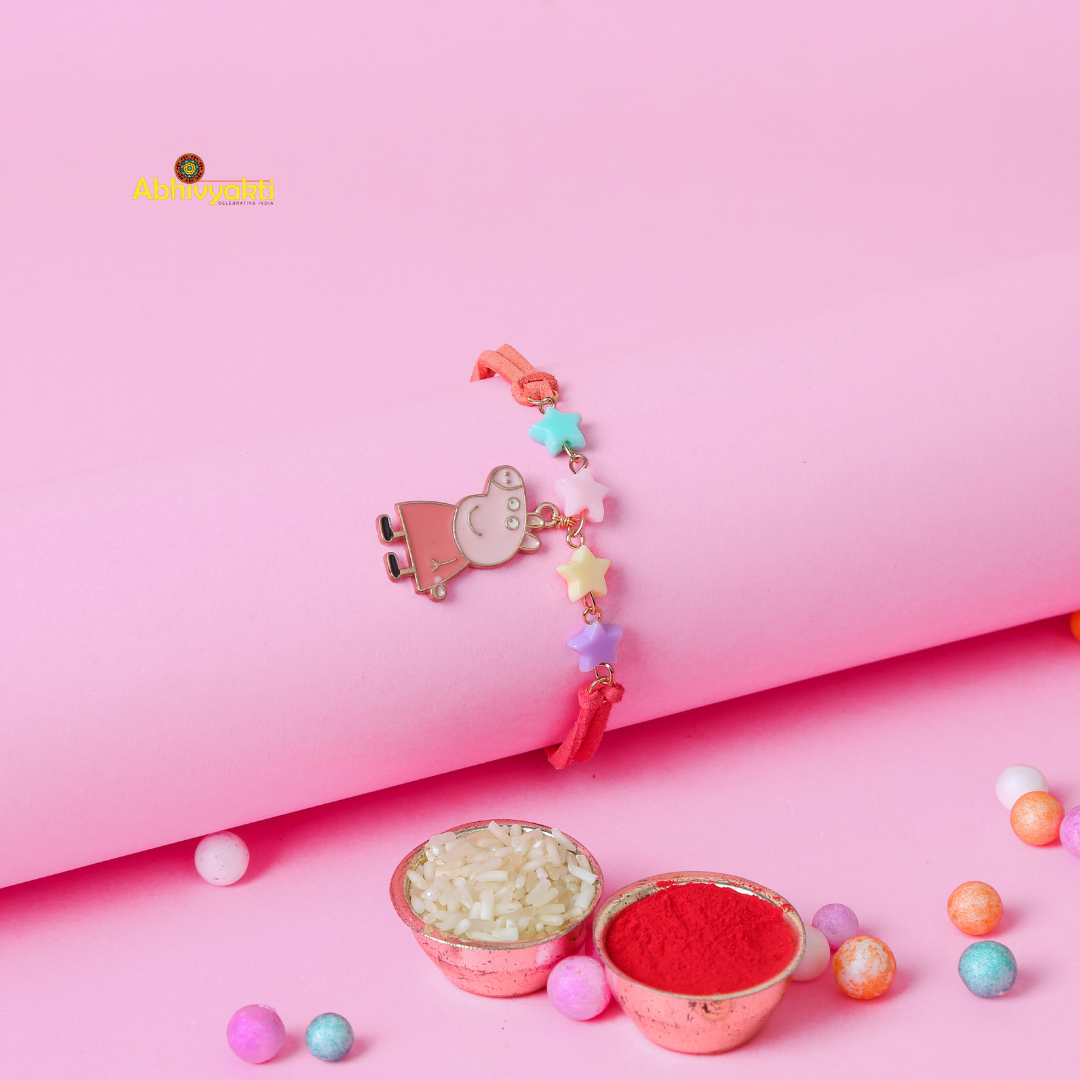 A children's bracelet laid on a pink background, featuring a charm of Peppa Pig in a pink dress and pastel-colored star beads in blue, yellow, pink, and purple. This adorable Peppa Pig rakhi for kids has a coral-colored band.