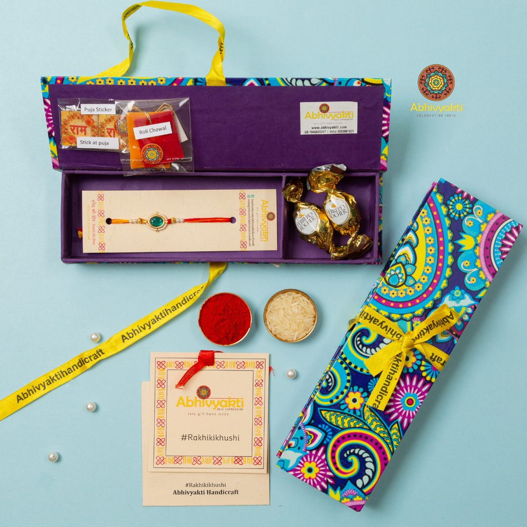 Traditional rakhi with an oval green stone centerpiece, surrounded by small pearls and gold accents, tied with red and yellow threads, with two small pouches, chocolates.