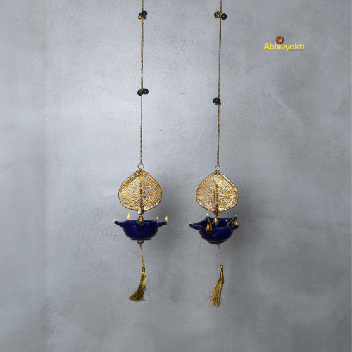 Two hanging decorative peacock swagata diya with gold and blue designs on a gray background