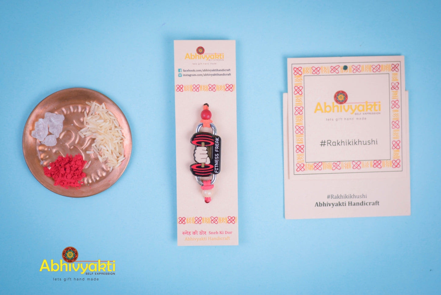 Fitness themed rakhi featuring a bold 'Fitness Freak' design with a dumbbell graphic on an orange thread, ideal for gym lovers, handcrafted with festive elements like rice, kumkum, and mishri.
