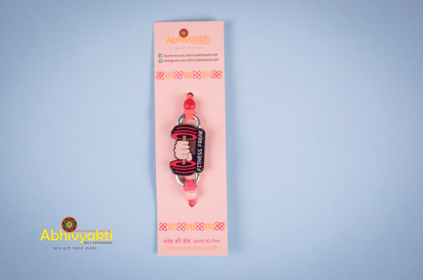 Fitness themed rakhi featuring a bold 'Fitness Freak' design with a dumbbell graphic on an orange thread, ideal for gym lovers.