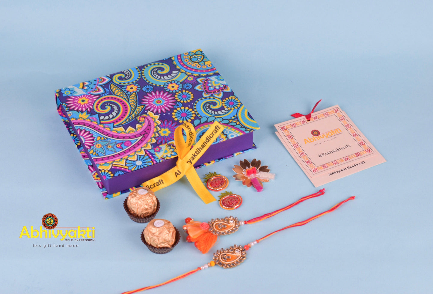Unique design orange rakhi and paisley lumba for bhaiya bhabhi with gold thread, tassels, stone, and beads.