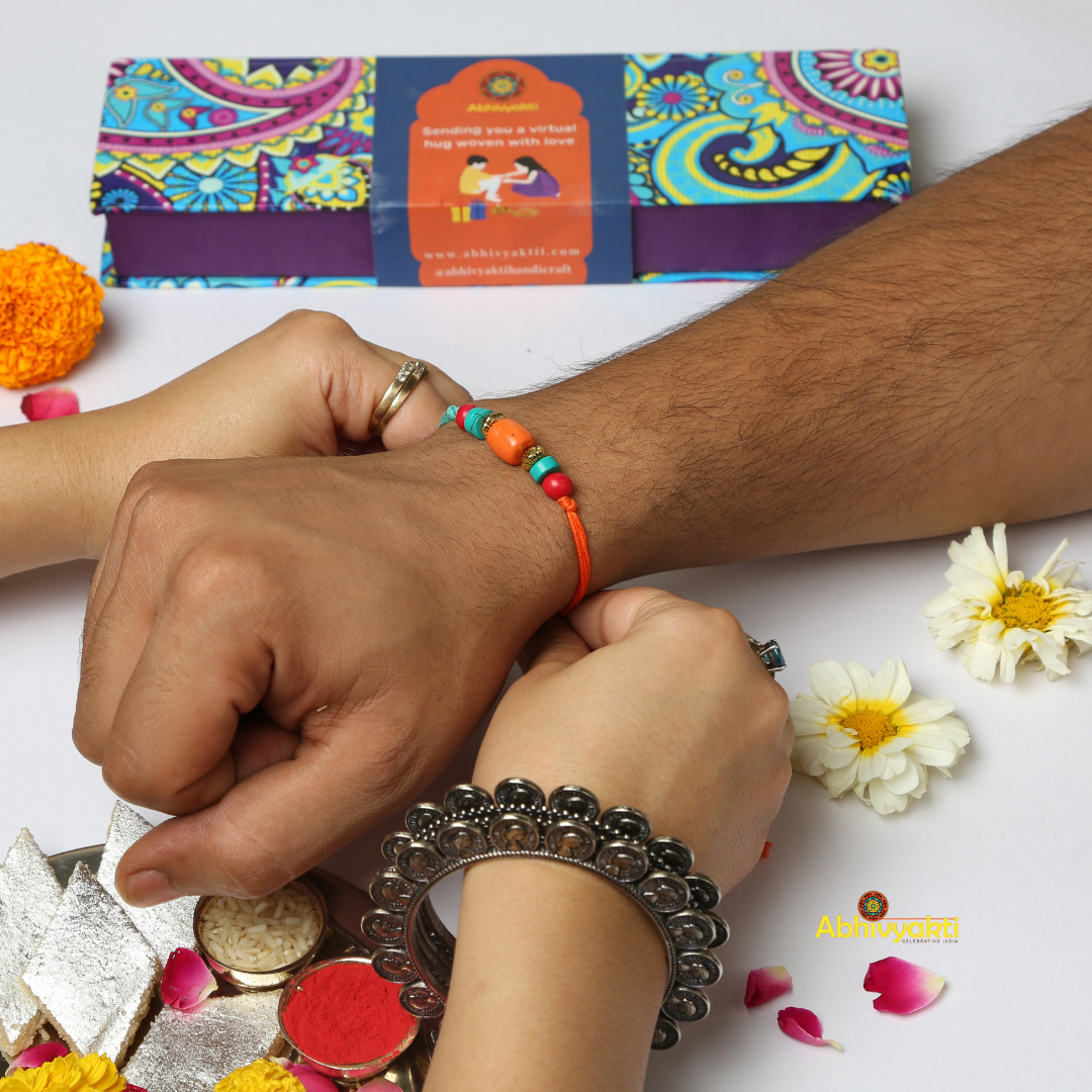 A colorful bracelet tied in wrist with orange and turquoise beads, along with gold spacers for your brother in this rakshabandhan