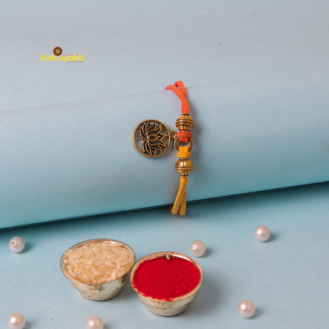 A decorative gold plated rakhi with a round lotus design in metallic gold, adorned with two additional gold beads