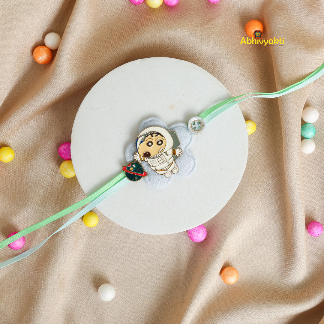 Vibrant Baby Astronaut Rakhi bracelet for kids, featuring a cute cartoon astronaut and spaceship charm on a pastel green thread, displayed on a soft beige background with colorful decorative balls.