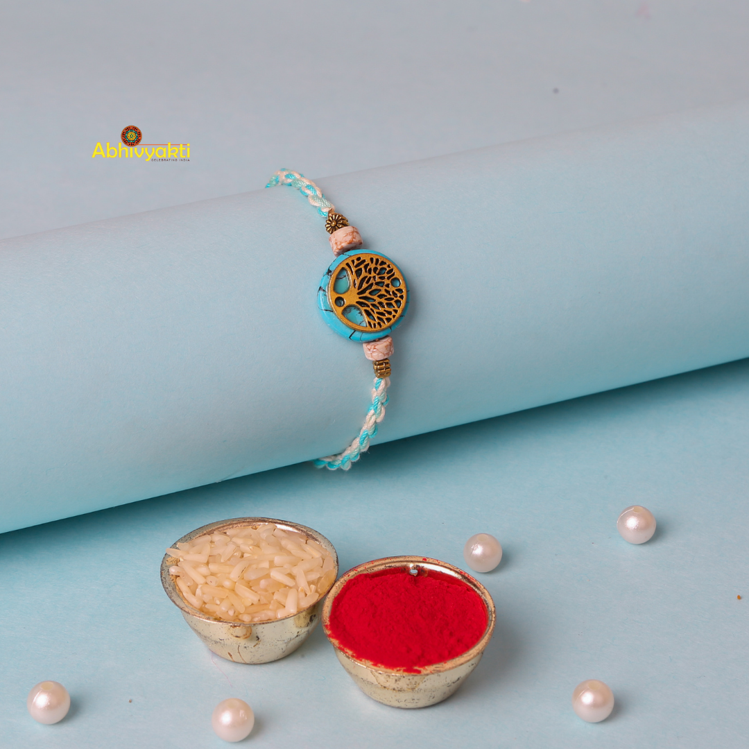 A braided bracelet with blue and white threads, featuring a circular charm with an intricate tree of life design in gold