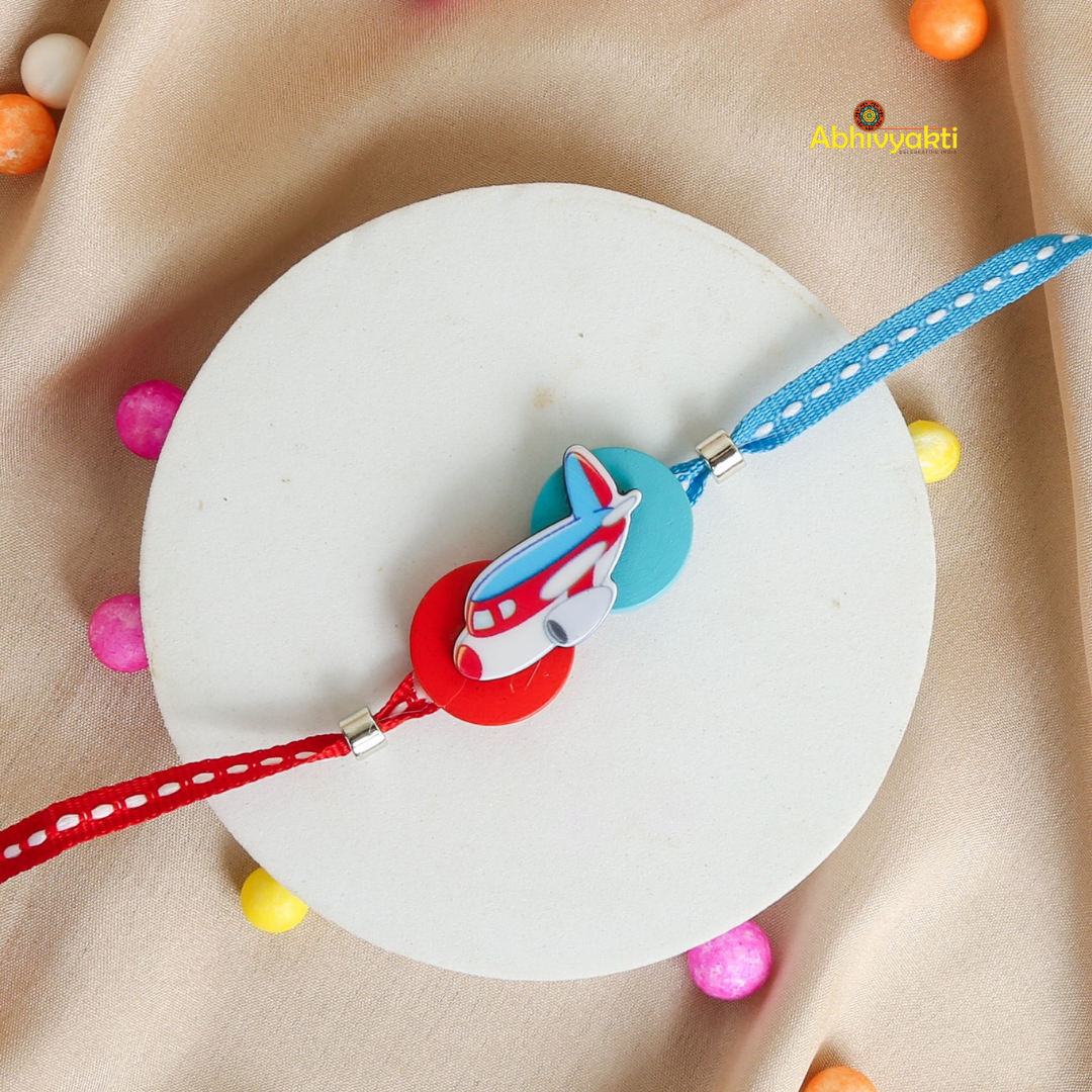 A blue and red Kids rakhi with a cartoon airplane charm and round beads is displayed on a white surface. 
