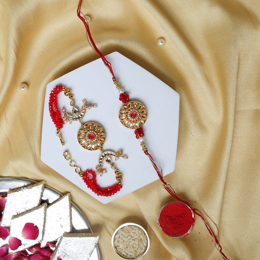 A decorative Rakhi and Lumba set with gold and red beads is displayed on a white hexagonal plate, surrounded by traditional Indian sweets, rice, and kumkum on a golden fabric background