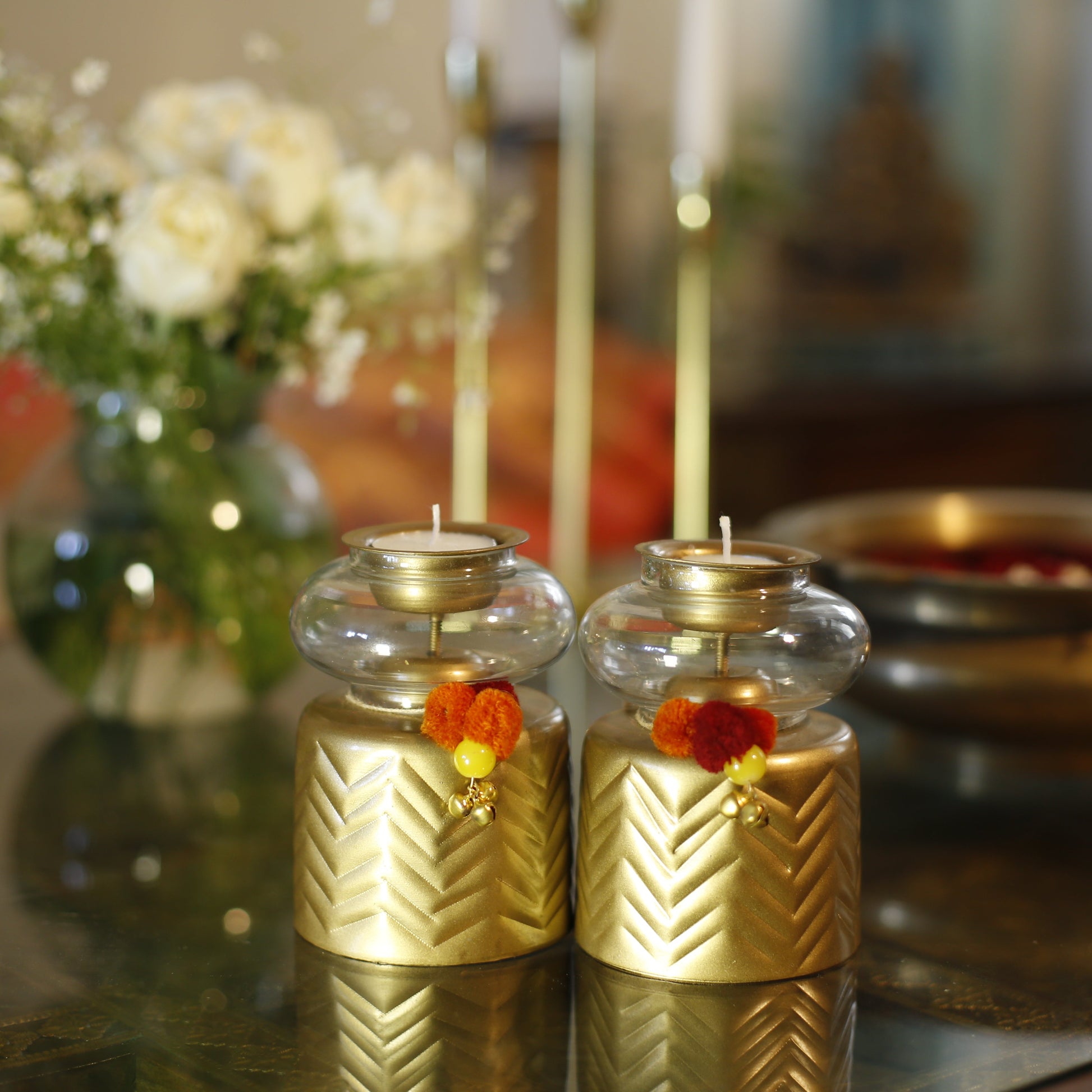 Anuya Tealight Holder Pair with flowers on a reflective surface, blurred background