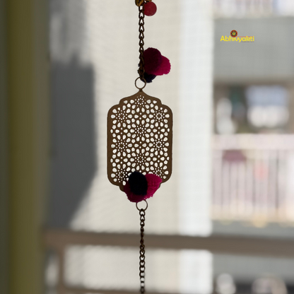 Filigree designed metallic door hanging with red and black pom-poms, suspended against a blurred background