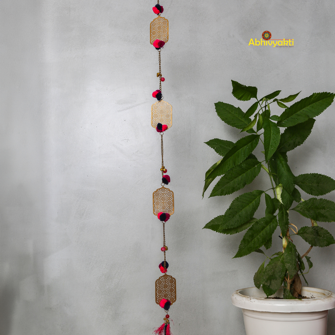 Filigree designed metallic door hanging with red and purple pom-poms, suspended against a light gray background