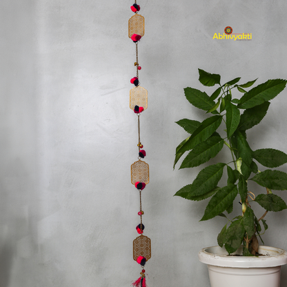 Filigree designed metallic door hanging with red and purple pom-poms, suspended against a light gray background