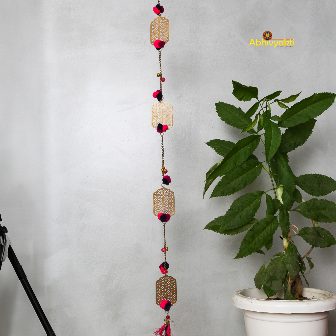 Filigree designed metallic door hanging with red and purple pom-poms, suspended against a light gray background