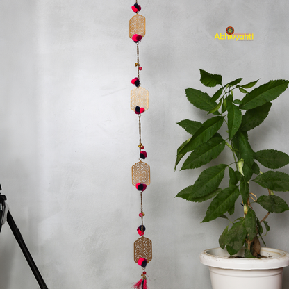 Filigree designed metallic door hanging with red and purple pom-poms, suspended against a light gray background
