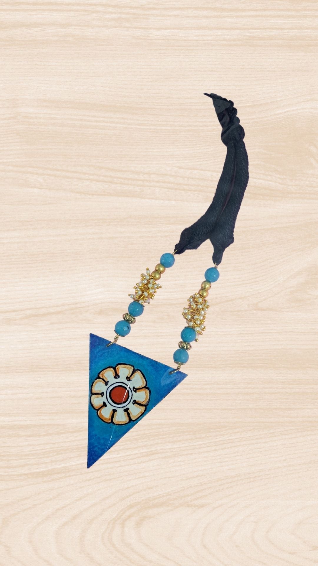 This beautiful Blue Triangle Adjustable Necklace with Wooden Pendant is hand painted and an exquisite Indian Jewellery inspired by Kerala Mural Art designed on crafted wood. It is surely an elegant wear for any occasion. A perfect head turner and a conversation starter..
