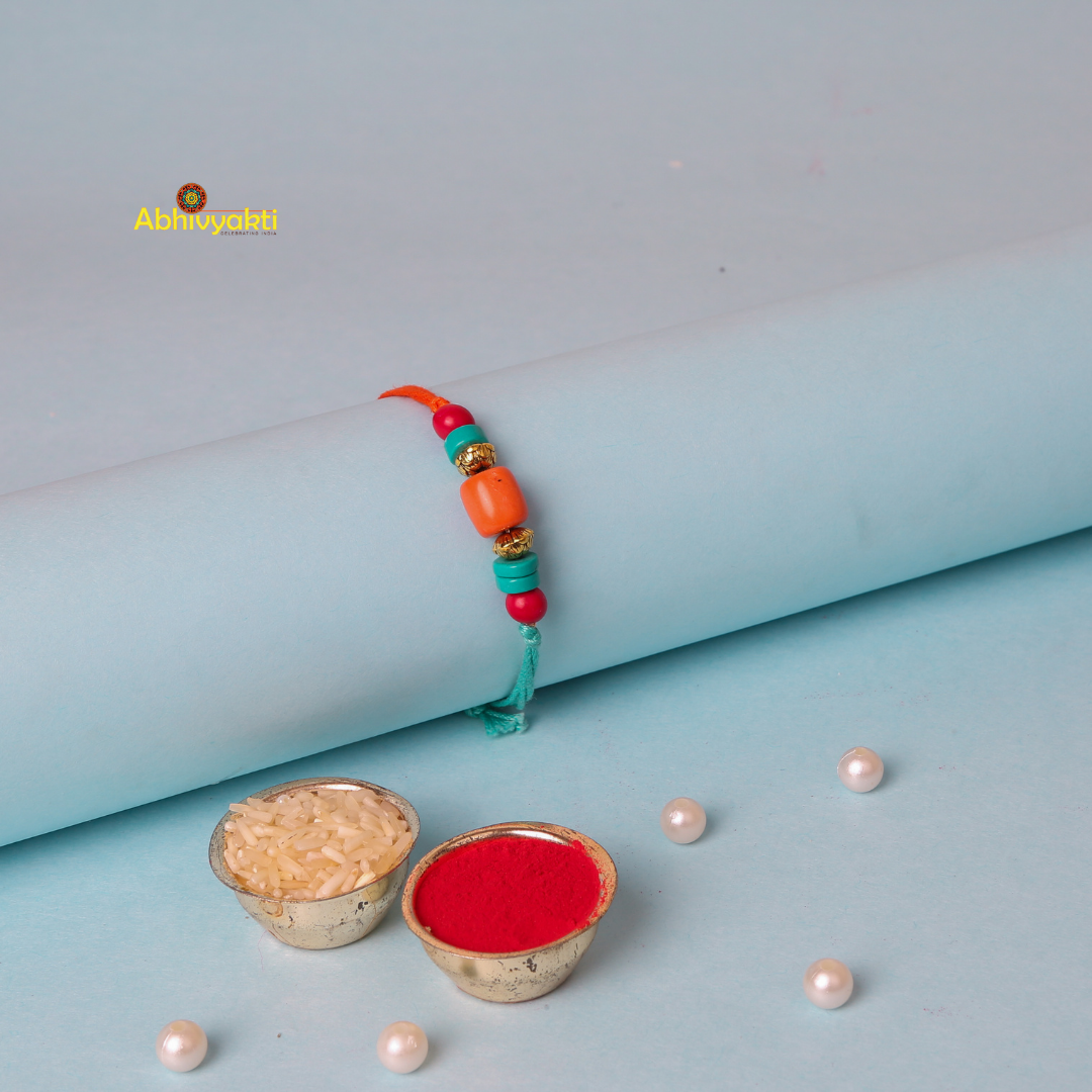 A colorful bracelet with orange and turquoise beads, along with gold spacers, is displayed on a light blue cylindrical object