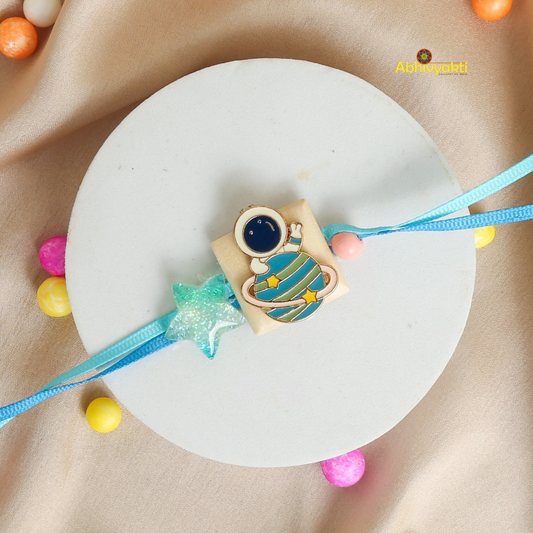 Cartoon astronaut and planet Rakhi bracelet for kids, featuring a blue strap, a glittery star, and a cute astronaut with a planet charm, displayed on a beige background with colorful balls.