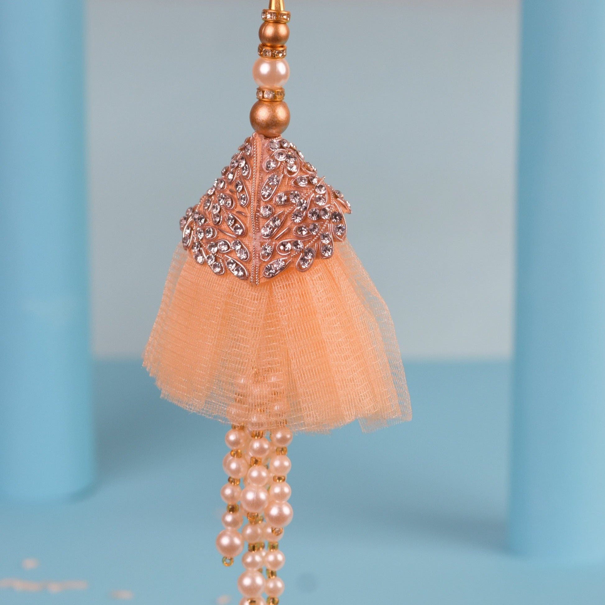 Elegant peach tassel against blue backdrop, embellished with stones and beads - rakhi lumba charm.