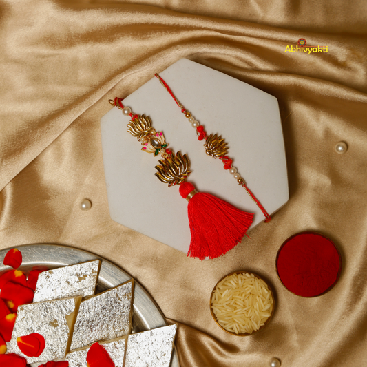 Two decorative rakhis lumba  with gold lotus-shaped charms and red beads, the other with gold lotus charms, white beads, a green gem, and a large red tassel, set against a golden background.