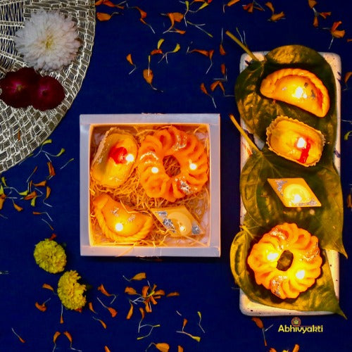Decorative, usable soy wax candles designed to resemble traditional Indian sweets like gujiya, peda, imarti, and barfi, beautifully arranged in a pastel green gift box with a transparent window.  ideal for gifting during Indian festival