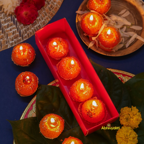 Decorative, usable soy wax candles shaped like traditional Indian sweets (motichoor ladoos), adorned with silver foil detailing, placed in festive packaging. Perfect for gifting and festive home decor