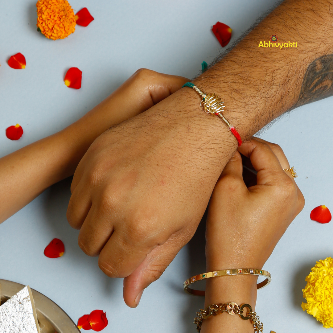 Elegant Rakhi featuring a golden lotus charm at the center, tied with contrasting red and teal threads. A minimal yet traditional design, perfect for celebrating Raksha Bandhan with a touch of symbolism and style