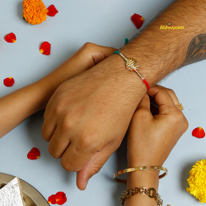 Elegant Rakhi featuring a golden lotus charm at the center, tied with contrasting red and teal threads. A minimal yet traditional design, perfect for celebrating Raksha Bandhan with a touch of symbolism and style