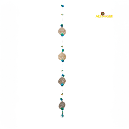 Filigree metal door hanging in a circular shape featuring detailed ornamental design, adorned with blue pom-poms and tiny golden bells, suspended from a chain indoors 