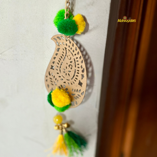 Filigree paisley-shaped metal door hanging adorned with yellow and green pom-poms and tassels, hanging on a white wall near a wooden door