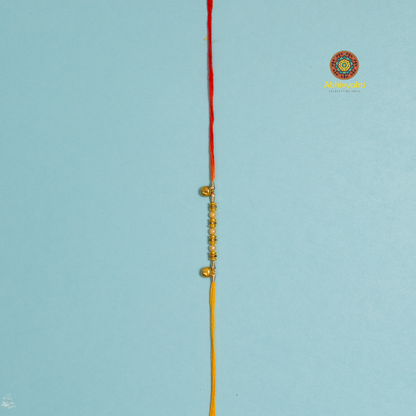 Golden bead and pearl rakhi on a yellow thread, wrapped around a blue roll, with bowls of rice and red kumkum powder, scattered pearls,  thread rakhi with beads and ghungru.