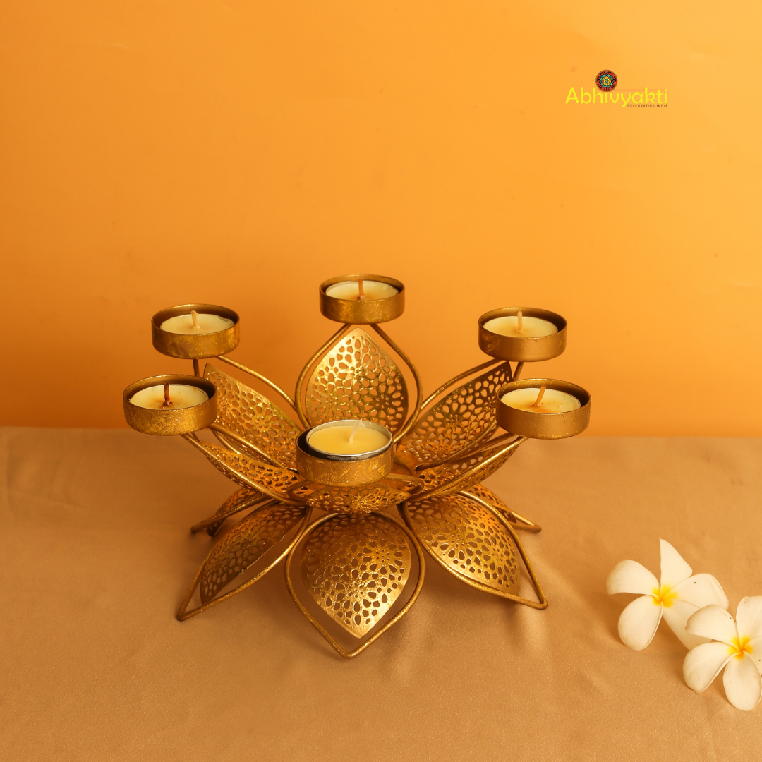 Golden metal padam t-light  holder in a flower shape with six intricate perforated petals, each petal holding a small round cup for candles, placed on a yellow background