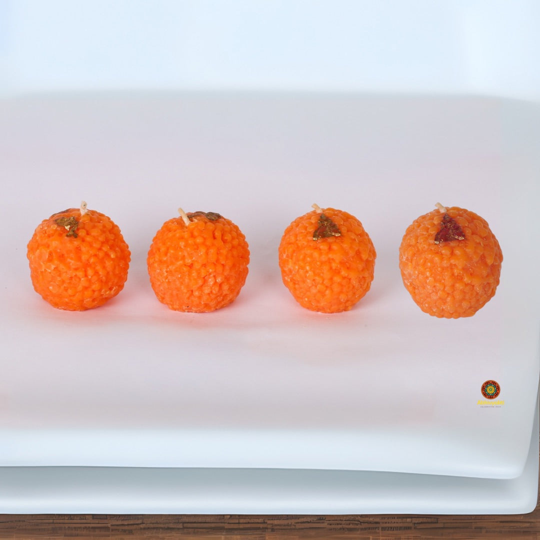 Decorative, usable soy wax candles shaped like traditional Indian sweets (motichoor ladoos), adorned with silver foil detailing, placed in festive packaging. Perfect for gifting and festive home decor
