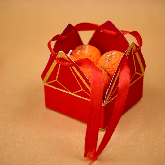 A beautifully designed candle box resembling a traditional Indian mithai (sweets) box. The box features bright, festive colors and intricate patterns, with multiple compartments holding candles shaped like popular Indian sweet, laddoo. Each candle has vibrant colors and detailed textures, evoking the look of real mithai, making it a perfect gift for festivals or special occasions.