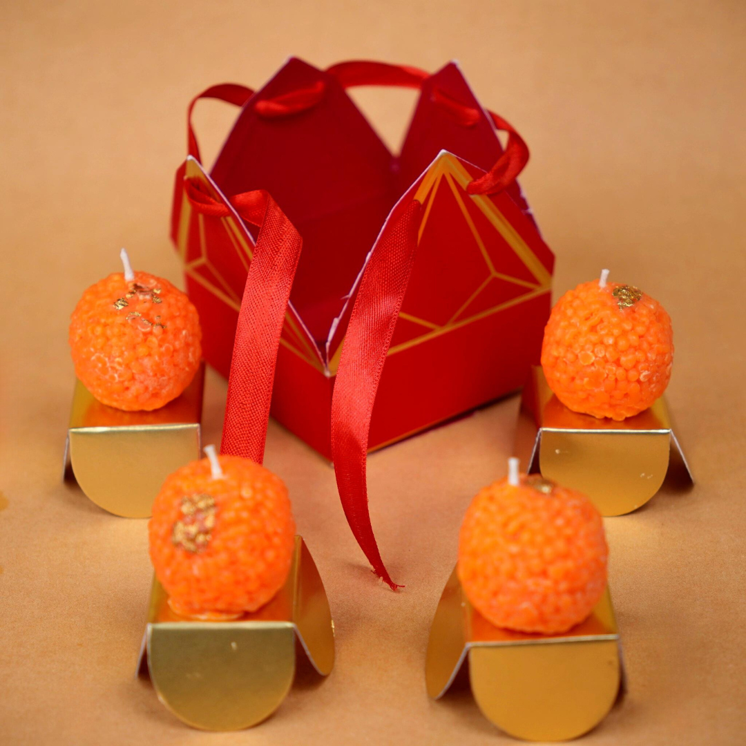 A beautifully designed candle box resembling a traditional Indian mithai (sweets) box. The box features bright, festive colors and intricate patterns, with multiple compartments holding candles shaped like popular Indian sweet, laddoo. Each candle has vibrant colors and detailed textures, evoking the look of real mithai, making it a perfect gift for festivals or special occasions.