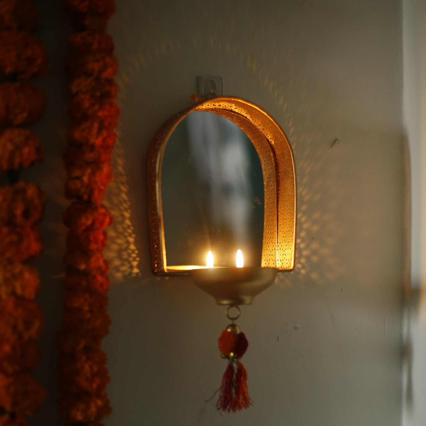 Decorative mirror tealight holder for Diwali decor with floral garlands on a plain background