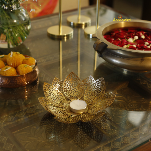 Decorative items including a gold lotus-shaped candle holder, small bowl with yellow items, and a pot with red flowers on a reflective surface.