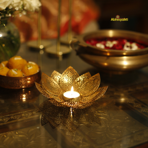 Decorative gold lotus-shaped candle holder with a lit candle on a reflective surface.