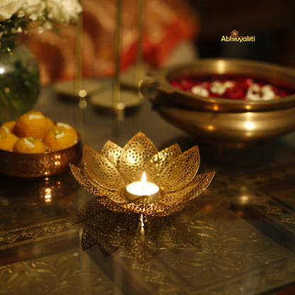 Decorative gold lotus-shaped candle holder with a lit candle on a reflective surface.